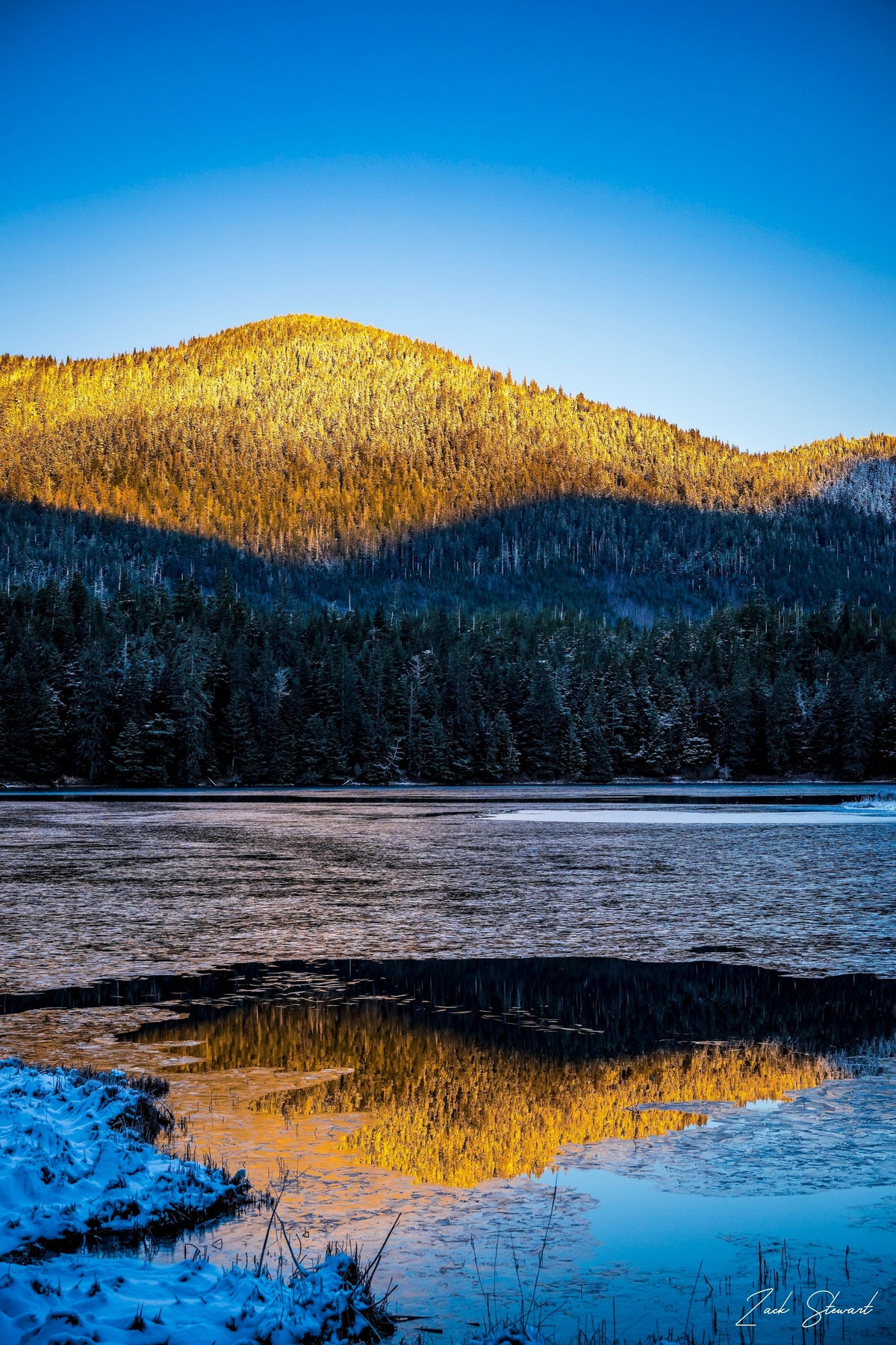 golden sun lights of the mountains of evergreen as it reflects in the icy lake below.